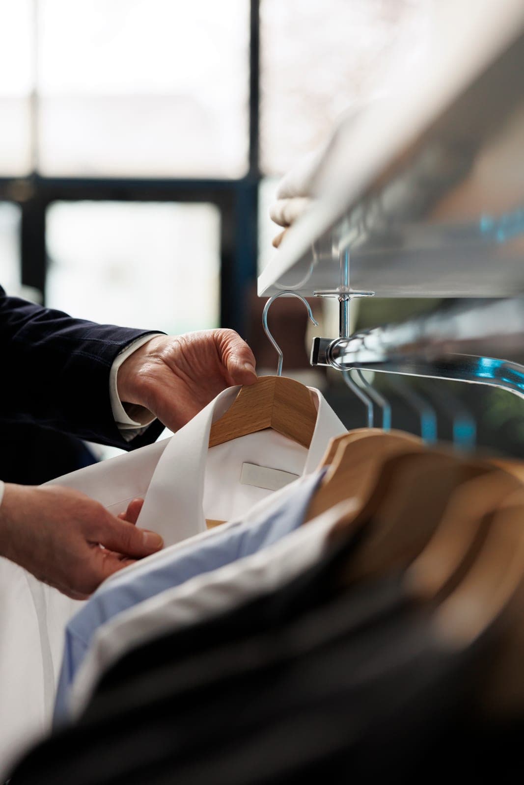 A freshly cleaned shirt being placed on a wooden hanger on a garment rail